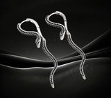 BKB Custom Gifts serpent hoop earrings with black stones and green eye accents on a dark abstract background
